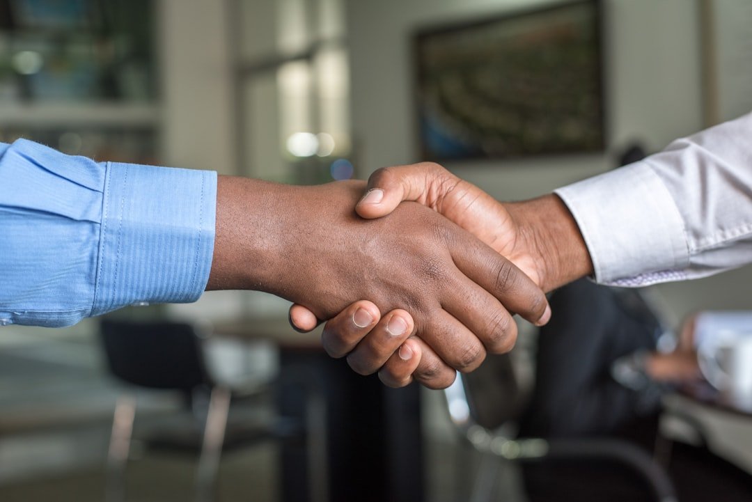 Two professionals shaking hands across a desk in a bright office meeting room