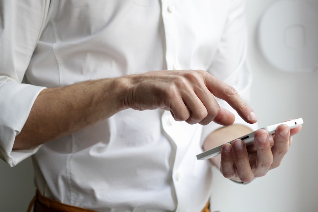 Person in a white shirt holding a white Android smartphone against a bright neutral background