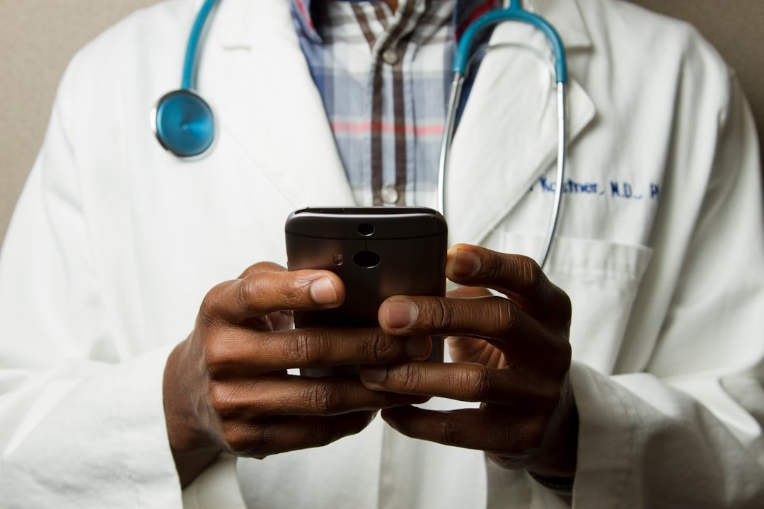 Healthcare professional in a gown with a stethoscope using a smartphone while standing