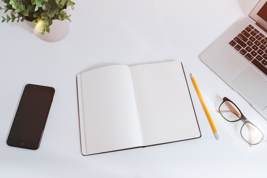 Open blank notebook beside an iPhone and a MacBook on a clean white work desk