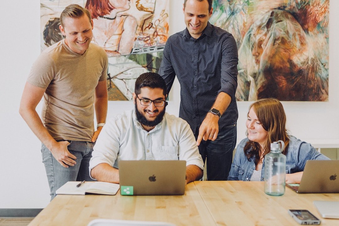 Four coworkers smiling and reviewing work together around a laptop at an office table