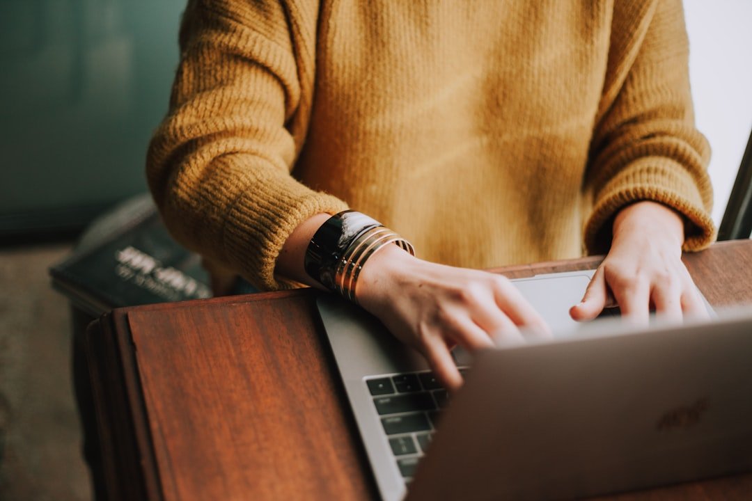 Person typing on a laptop at a dark wooden desk, side-lit in warm tones