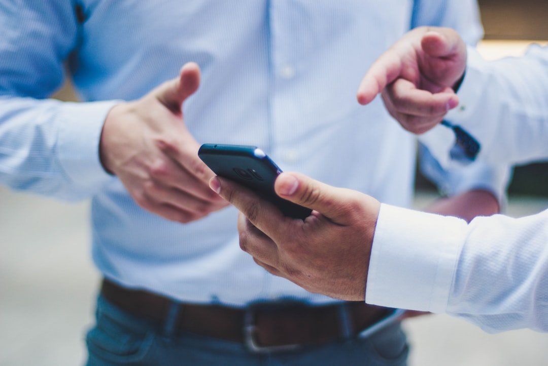 Two professionals in business shirts discussing a smartphone screen, one holding the device and the other pointing at it